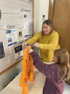 A parent and her daughter working together to stack cups using a rubber band tool