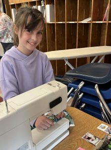 4-Her using a sewing machine while smiling at the camera