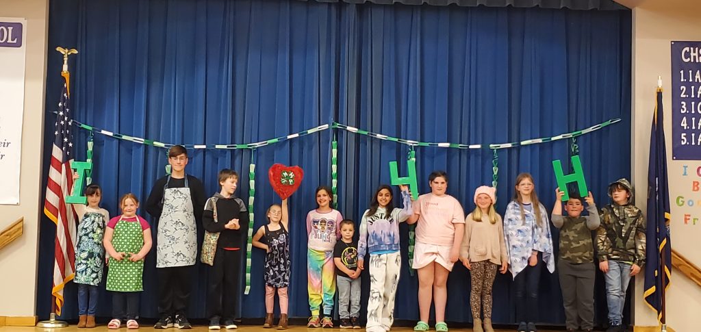 4-H Style Revue participants on stage in their garments holding up an "I Heart 4-H" sign