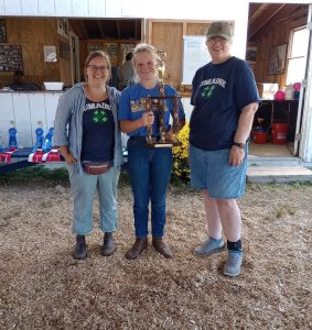 4-H staff, Carla, standing with Razor Crosman Award winner, Amelia, and 4-H Volunteer Terry. Amelia is holding her trophy