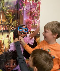 Two 4-H youth using photobooth props to give movie characters a funny outfit on an Encanto poster