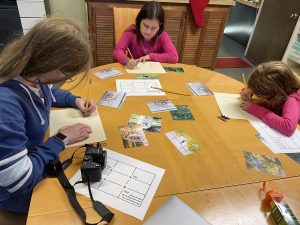 Three youth gathered around a table drawing on paper. In the middle of the table is a bunch of photos printed out with grids drawn on them.