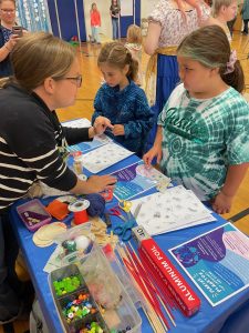 4-H Staff explaining a workshop activity to two youth listening intently.