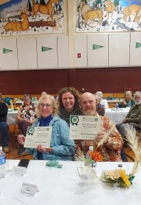 Leah with Becky and Norwood receiving their awards. There are smiling onlookers in the background. 