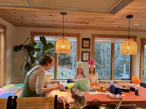 Three youth around a table full of craft supplies and an adult talking to them