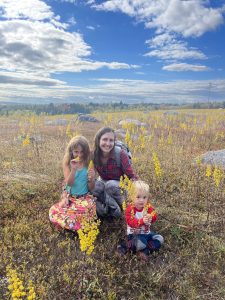 Two kids with their mom smiling at the camera in a rocky field of yellow flowers