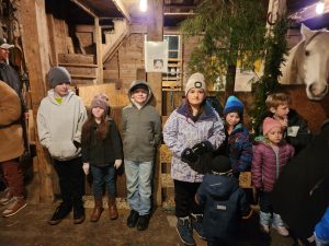 Youth lined up in front of the hose stable smiling at the camera. A friendly horse head pokes out above them.