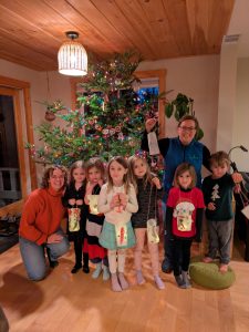 Youth and club leaders smiling in front of a Christmas tree. The youth are holing up paper lanterns they made.