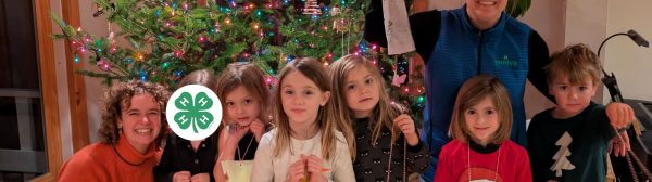 Youth and club leaders smiling in front of a Christmas tree. The youth are holing up paper lanterns they made.