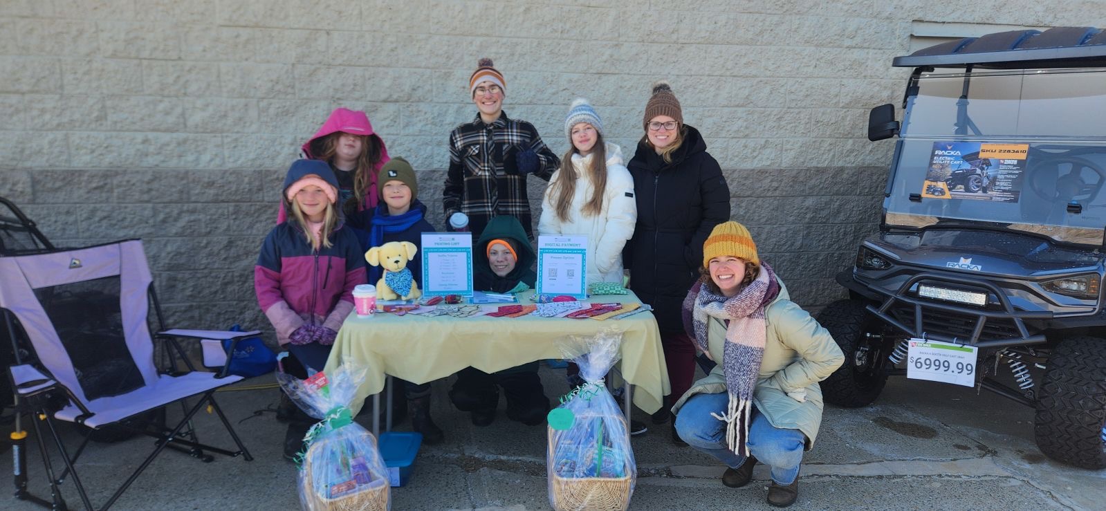 Youth dressed for cold weather in front of a table filled with raffle baskets and dog bandanas