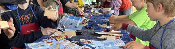 Side view along a wooden picnic table with youth along either side each woking on a building project in front of them.