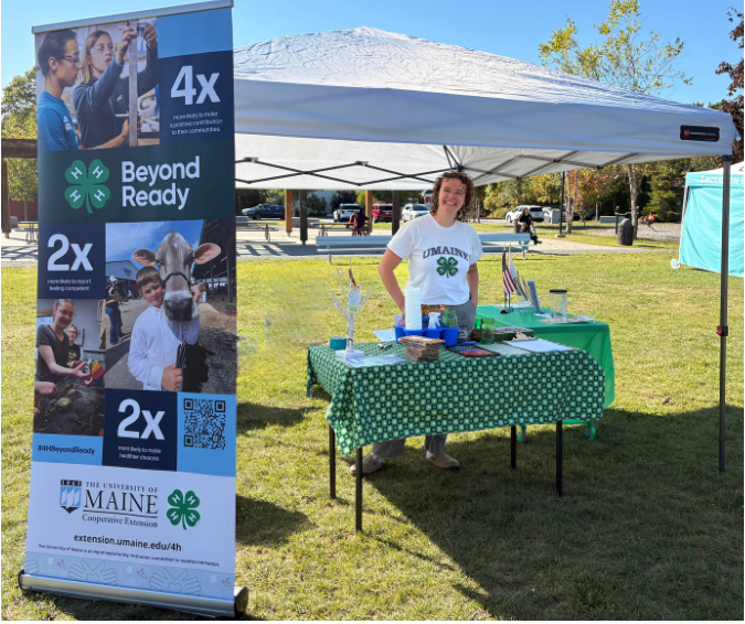Leah, 4-H Professional, standing with a 4-H banner at an event