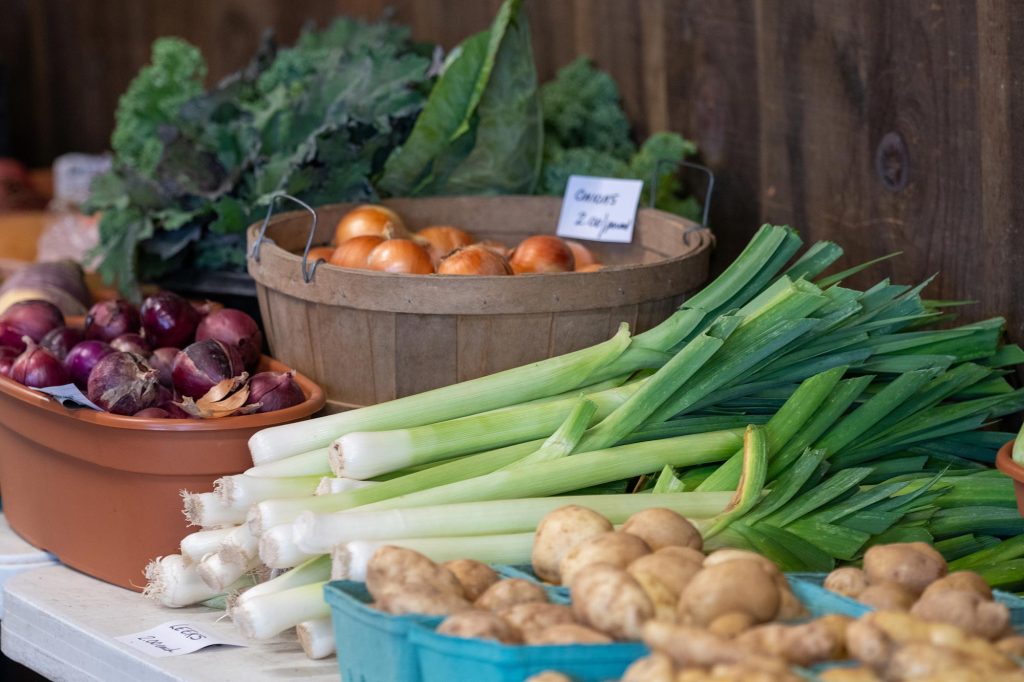 table of various vegetables including red and yellow onions, potatoes, and leeks