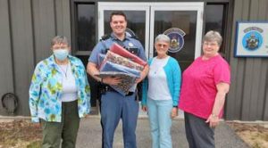 three women standing with a state policemen who has received quilts that they've made