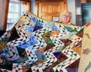 a woman holding up a hand-made quilt