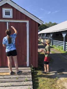 Two children painting a small, red building