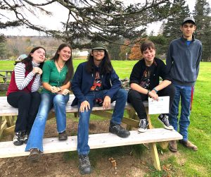 5 teens sitting on or near a picnic table outside