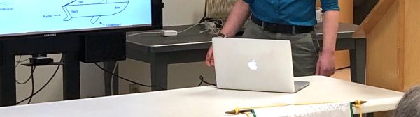 Young person standing behind a table looking at a screen while presenting a talk