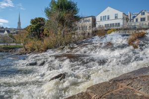 sunny outdoor scene of trees and buildings directly above a waterfall cascading over levels of rock and ledge