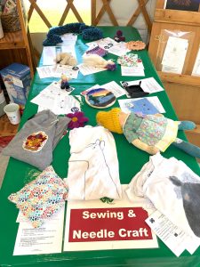 green table with t-shirts, dolls and objects made with fabric, yarn, and wool by 4-H youth