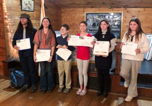 Six young people standing in front of a stage holding certificates