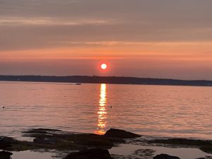 sun setting over water with a passing boat in the distance, rocks in the foreground