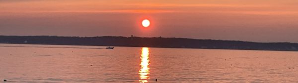 sun setting over water with a passing boat in the distance, rocks in the foreground