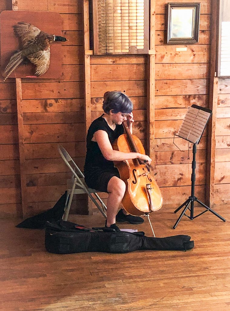 Young woman in black dress sitting on chair playing cello in a rustic wooden building