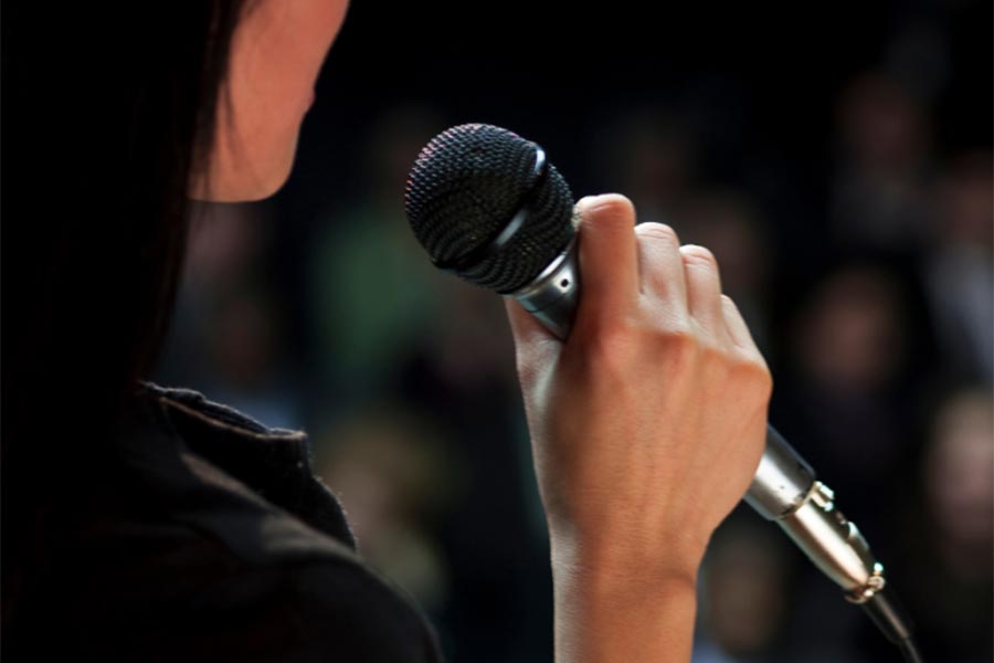 a person holding a microphone to their mouth speaking in front of a crowd
