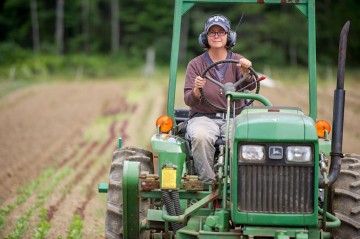 woman wearing ear protection riding on a tractor in a garden