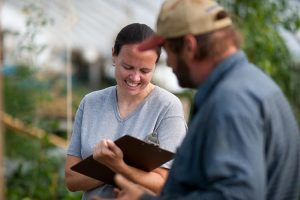 instructor with a clipboard working with a farmer in a greenhouse