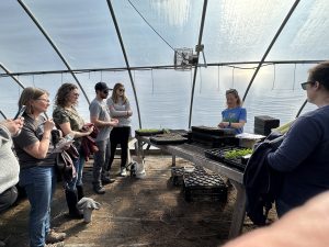 group of people watching a farmer plant seeds in trays in a greenhouse