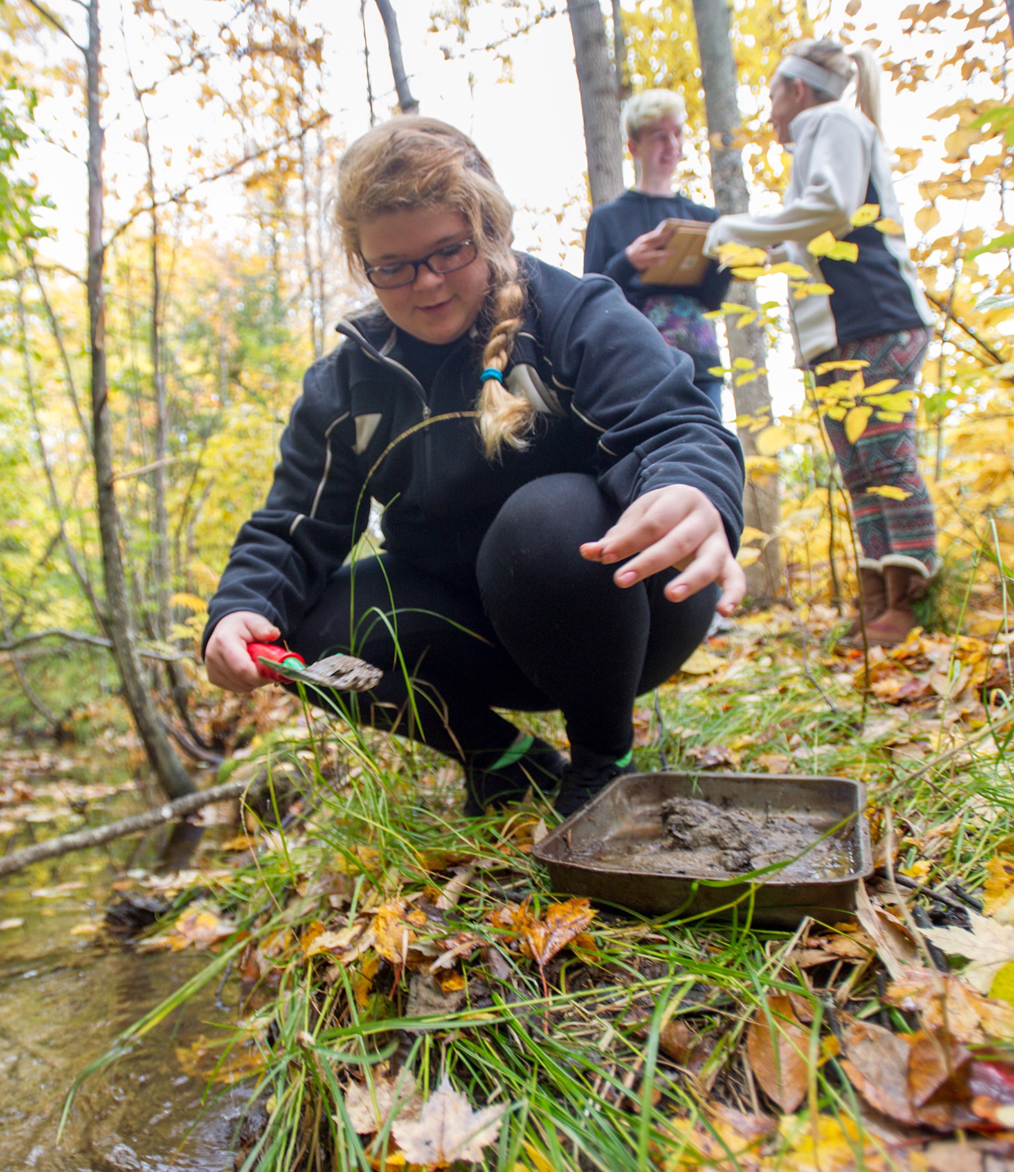a pre-teen taking soil samples from a stream in the forest