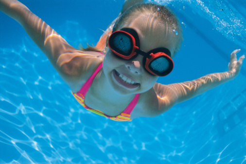 girl with swimming goggles under water in pool