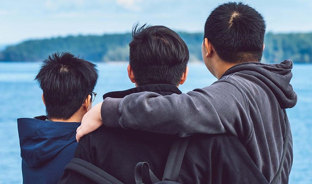 three teenagers with their arms around one another looking out to the ocean
