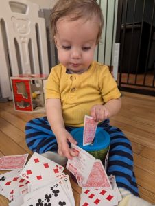 young child trying to put cards in a can