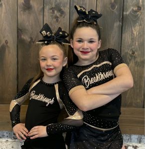 2 youth cheerleaders dressed in black against a brown wall