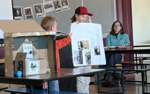 youth standing at table showing a demonstration holding a poster