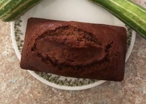 loaf of Zucchini bread on a plate with two zucchini squash on the side