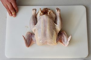 Photo of whole, raw chicken on a cutting board.