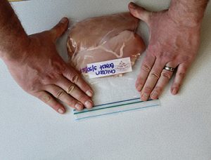 Photo showing inserting chicken pieces into a freezer resealable bag for storing and closing the bag.