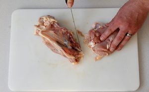 Photo of raw chicken and a knife passing through the wing joint where the tenderloin tendon connects to the body.