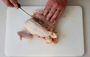 Photo showing whole raw chicken and to start on one side of the keel bone and follow the curve of the ribs to remove the breast meat from the body.