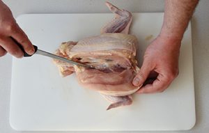 Photo of raw chicken and a knife passing through the wing joint where the tenderloin tendon connects to the body.