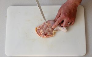 Photo of raw chicken and hwo to separate the thigh and drumstick place skin side down on cutting board. Look for the line of fat between the leg and thigh.