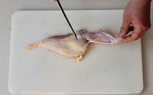 Photo of raw chicken and how to remove a wing by cutting it away from the breast.