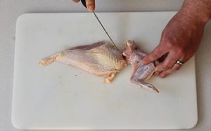 Photo of raw chicken and how to remove a wing by cutting it away from the breast.