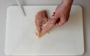 Photo of raw chicken and how too remove the tenderloin, place the chicken breast skin side down and peel the tenderloin away from the breast.