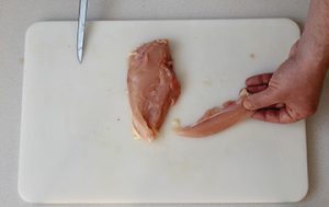 Photo of raw chicken and how too remove the tenderloin, place the chicken breast skin side down and peel the tenderloin away from the breast.