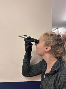 The female is holding a refractometer with her right hand up to her eye.